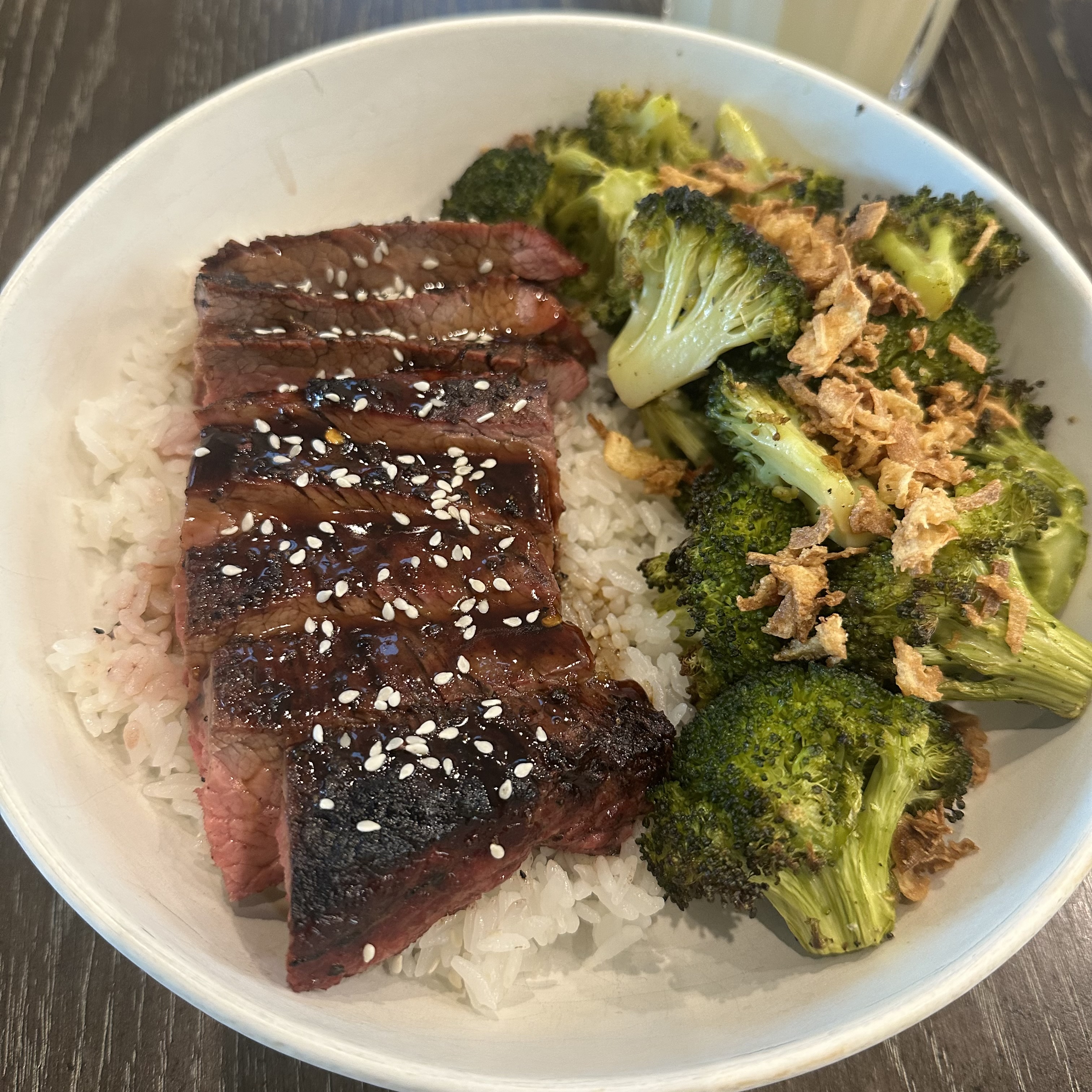 Grilled flank steak with teriyaki on a bed of rice and broccoli. Topped with fried shallots and sesame seeds.